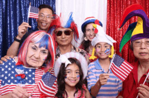 Family and friends wearing patriotic costumes and holding American flags while posing together in a festive photo booth.