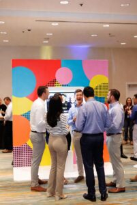 Corporate event attendees gathered around a colorful interactive photo booth during a business networking event.
